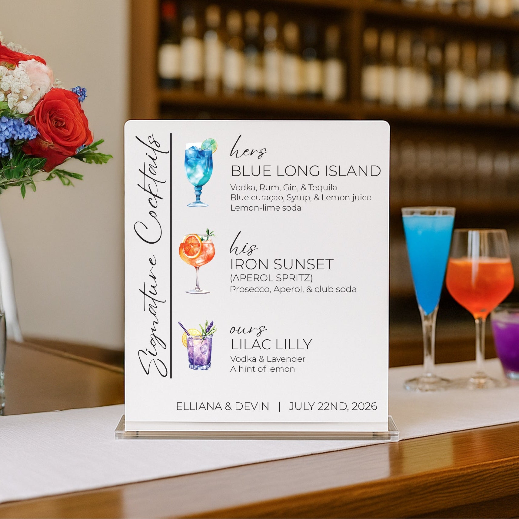 A custom cocktail menu sign displayed on a bar counter in a restaurant setting, with a blurred background of wine bottles and colorful cocktails in glasses.
